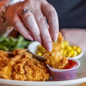 Hand-dipping crispy chicken tenders into barbecue sauce