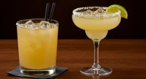 Hurricane Margarita at Texas Roadhouse with red-orange layers, lime and cherry garnish, and sugared rim on a wooden table.