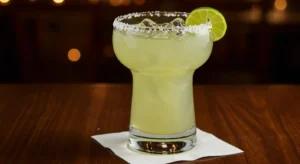 Original House Margarita from Texas Roadhouse served over ice with salted rim and lime wedge on a wooden table.