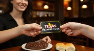 Guest handing a Texas Roadhouse gift card to a smiling server at a table with steak