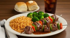 Hearty plate with Texas Roadhouse-style steak kabobs, grilled vegetables, seasoned rice, and a side of broccoli, served with a dinner roll and iced tea