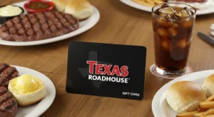 Texas Roadhouse gift card with official logo on a rustic table surrounded by steak, rolls, and a drink