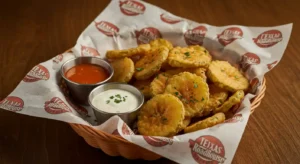 Basket of crispy fried pickle chips with ranch and Cajun dipping sauces.